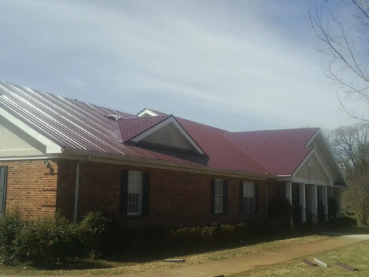 Red metal roof with gabled entries on a long brick building, from a Hail Damage Roof Repair job in Venus